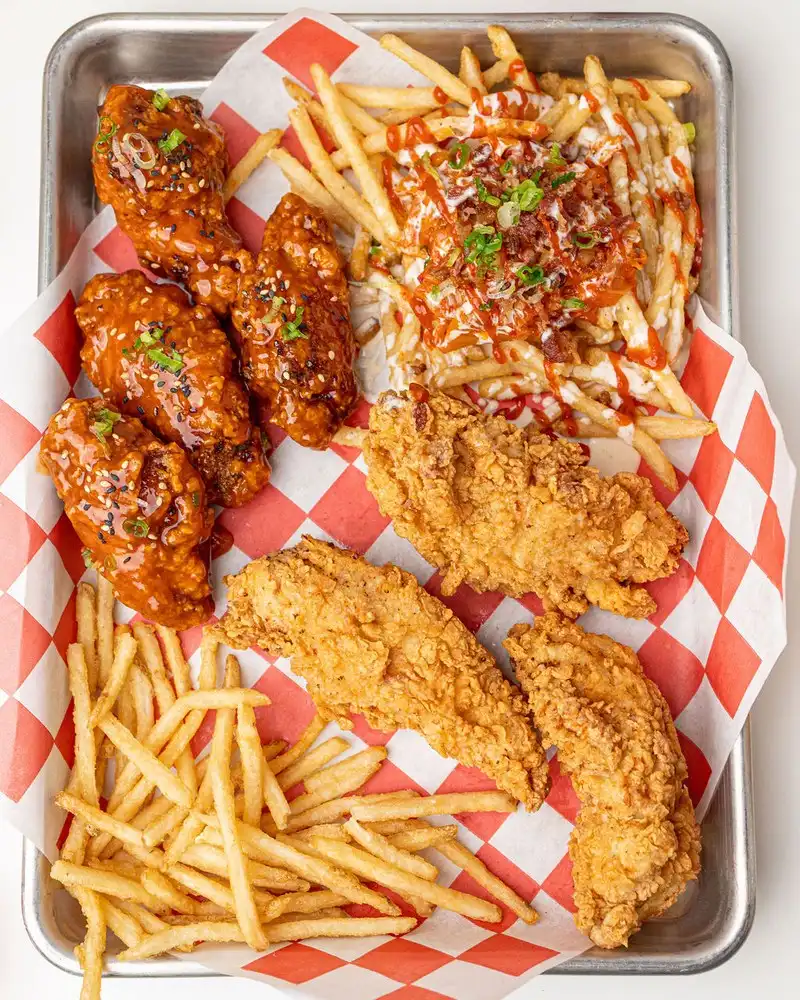 A tray of Korean fried wings glazed in sweet & spicy sauce, golden chicken tenders and loaded fries